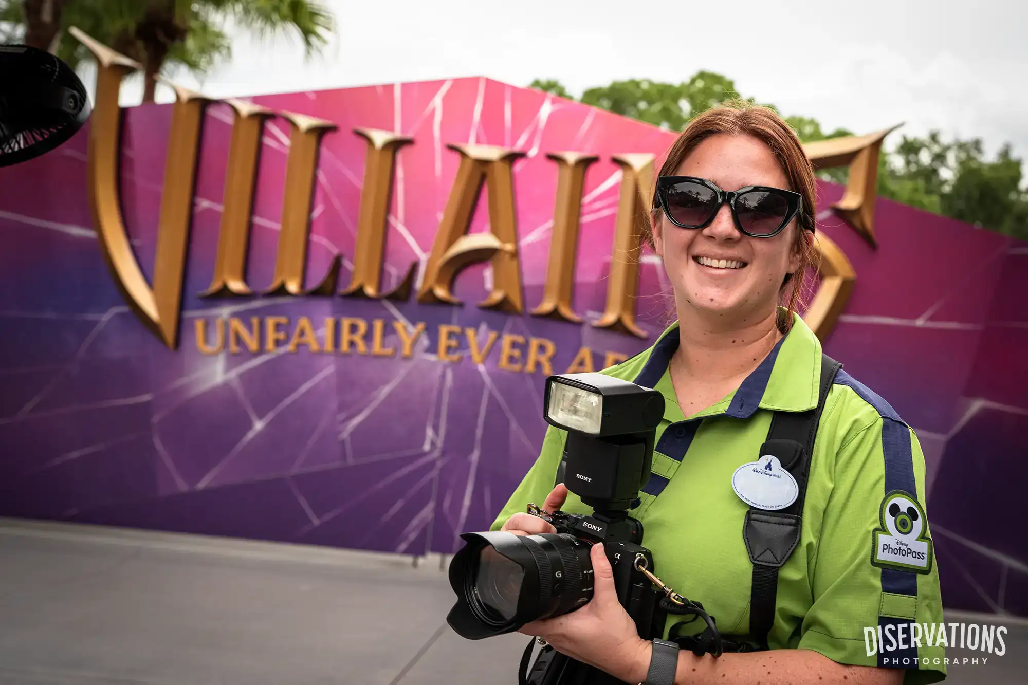 A Disney Cast Member photographer in front of the Villains Unfairly Ever After sign